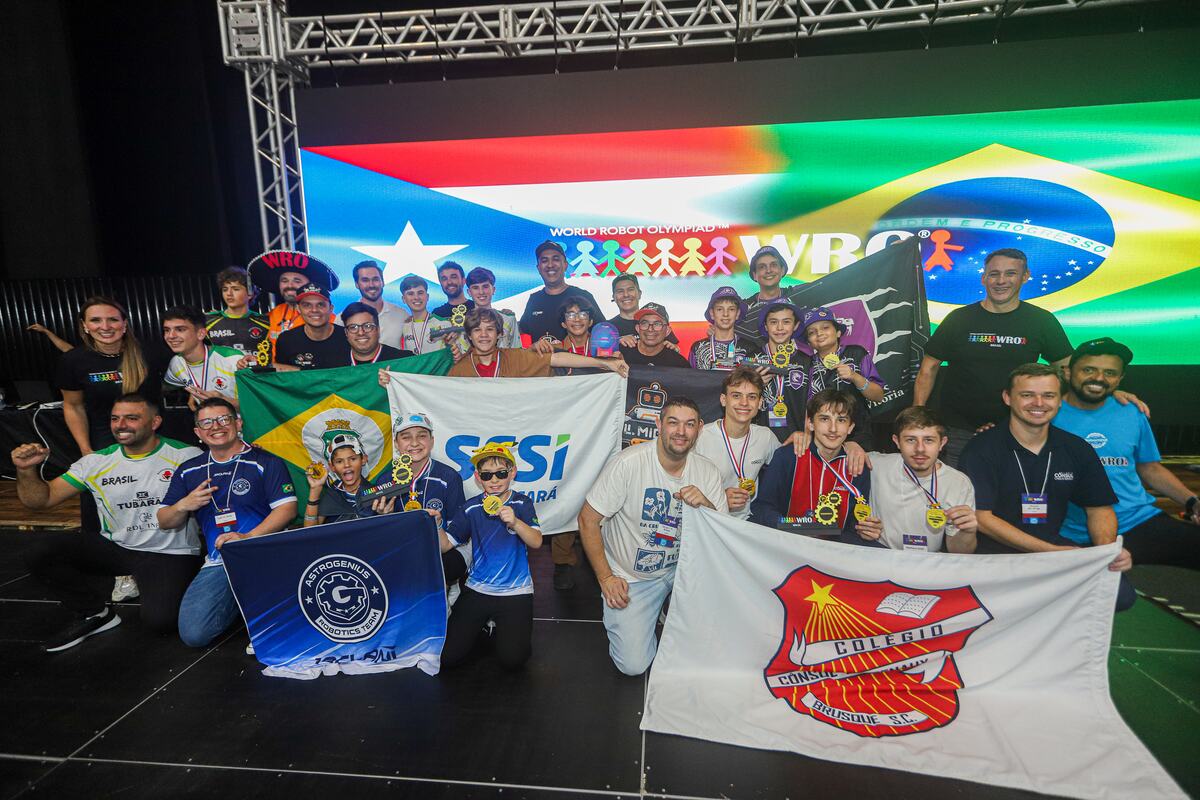 Equipe brasileira comemorando no palco da WRO Brasil com bandeiras e medalhas